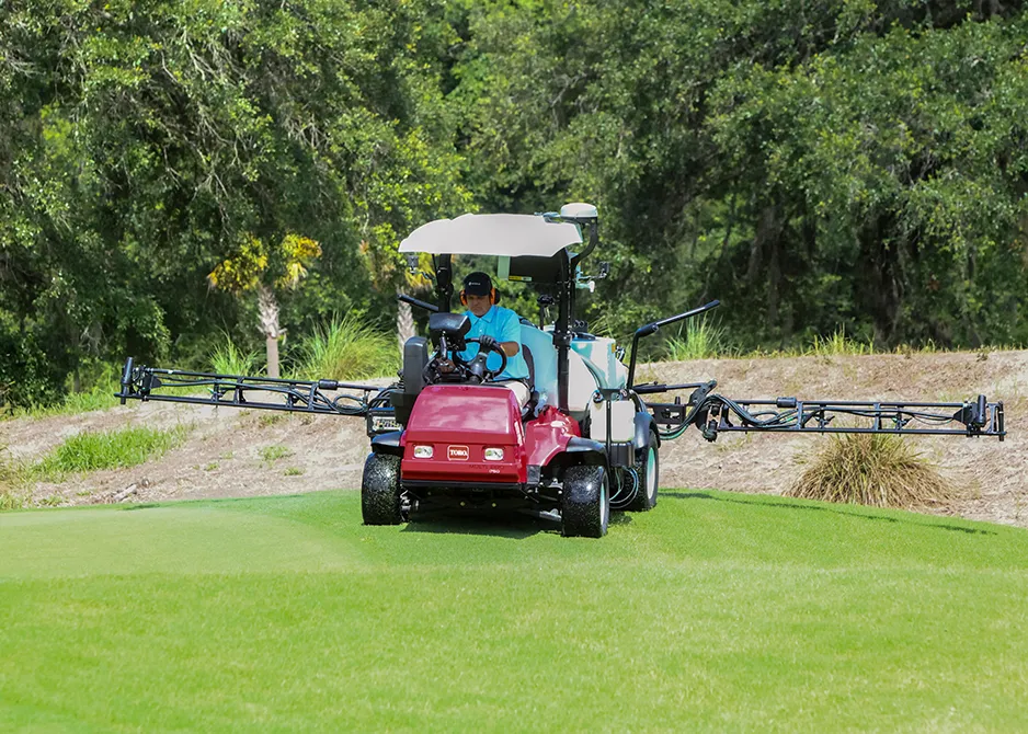 Golf course spray technician driving a wide-boom sprayer with extended arms across a green.